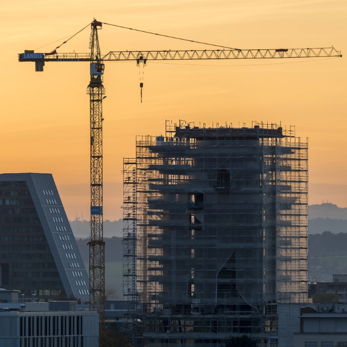 Ein eingerüstetes Hochhaus mit einem Baukran im Abendrot.